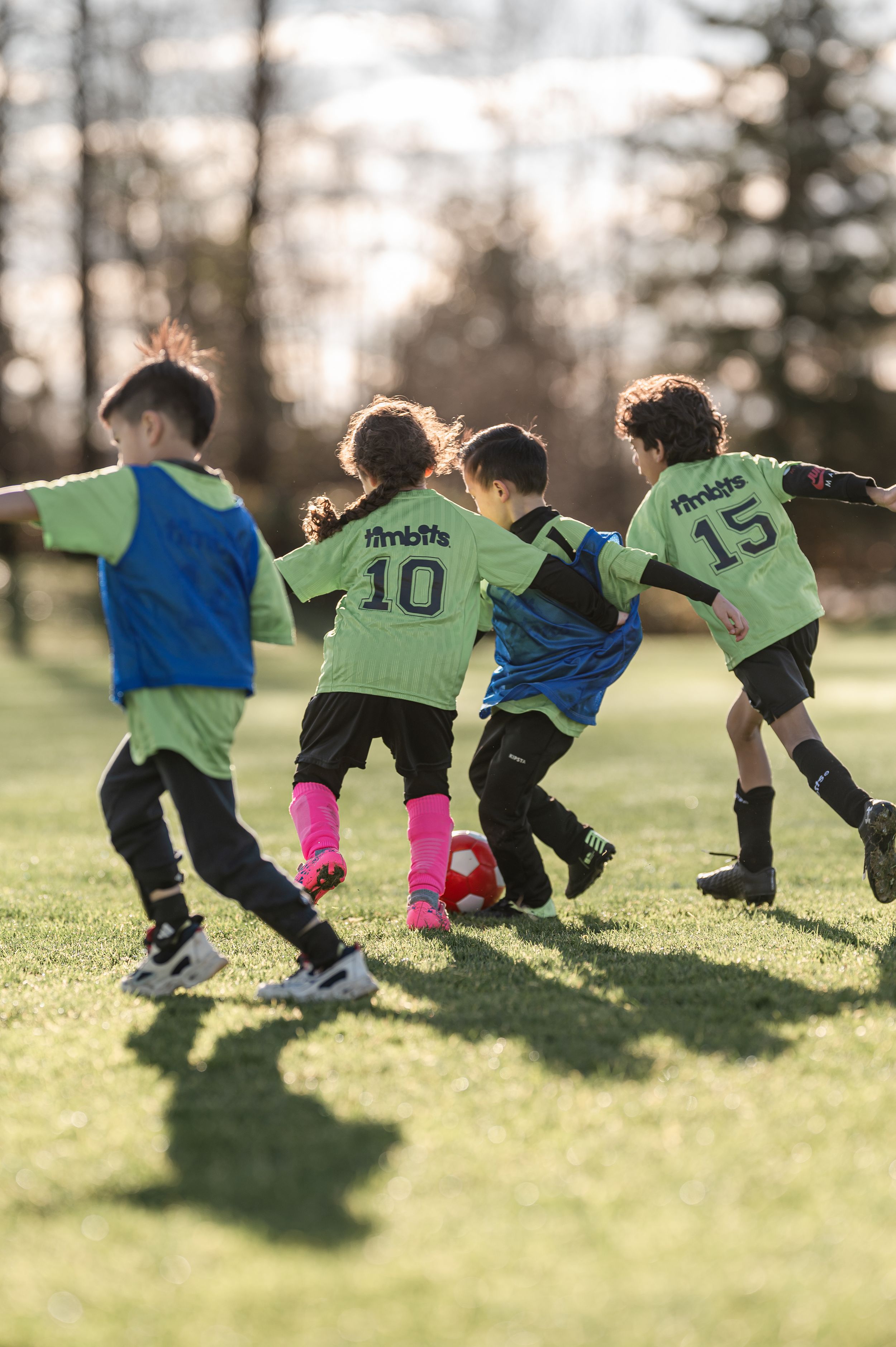 Young children in green jerseys compete for a soccer ball during an outdoor youth football match on a grass field.