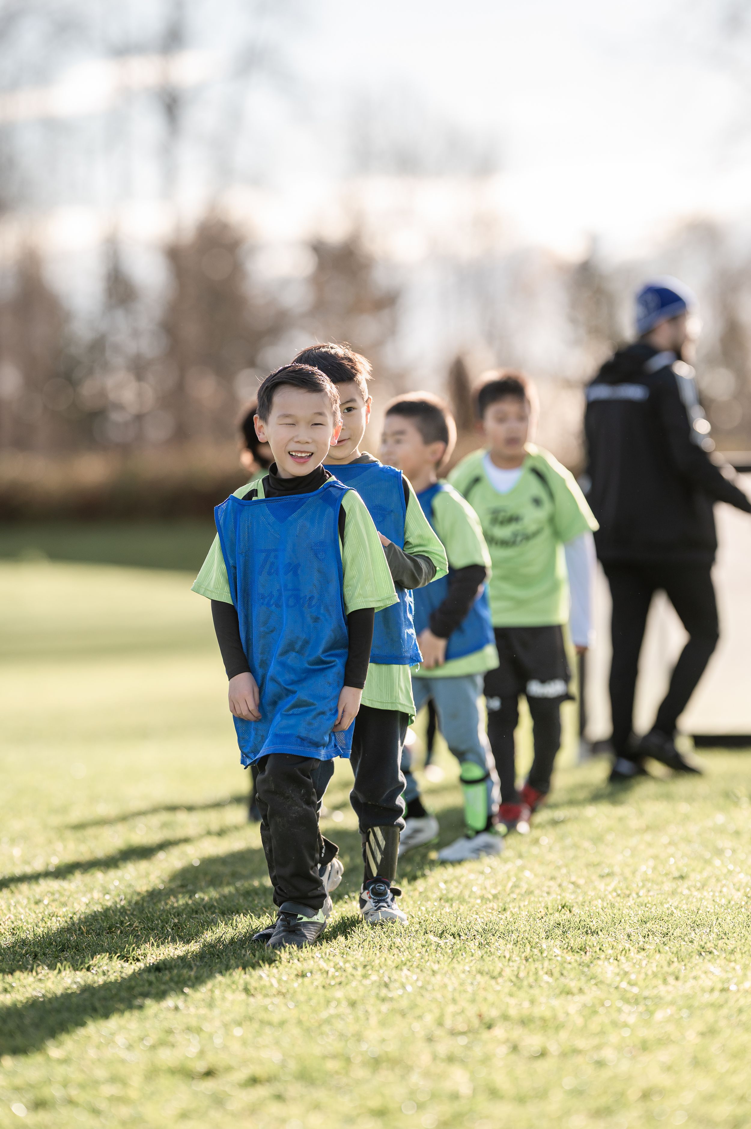 Young boys in green and blue soccer jerseys line up on a grass field during a youth football training session.