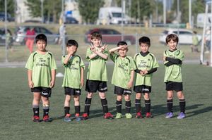 Six young children in matching green soccer uniforms pose together on a grass field during a youth soccer game.