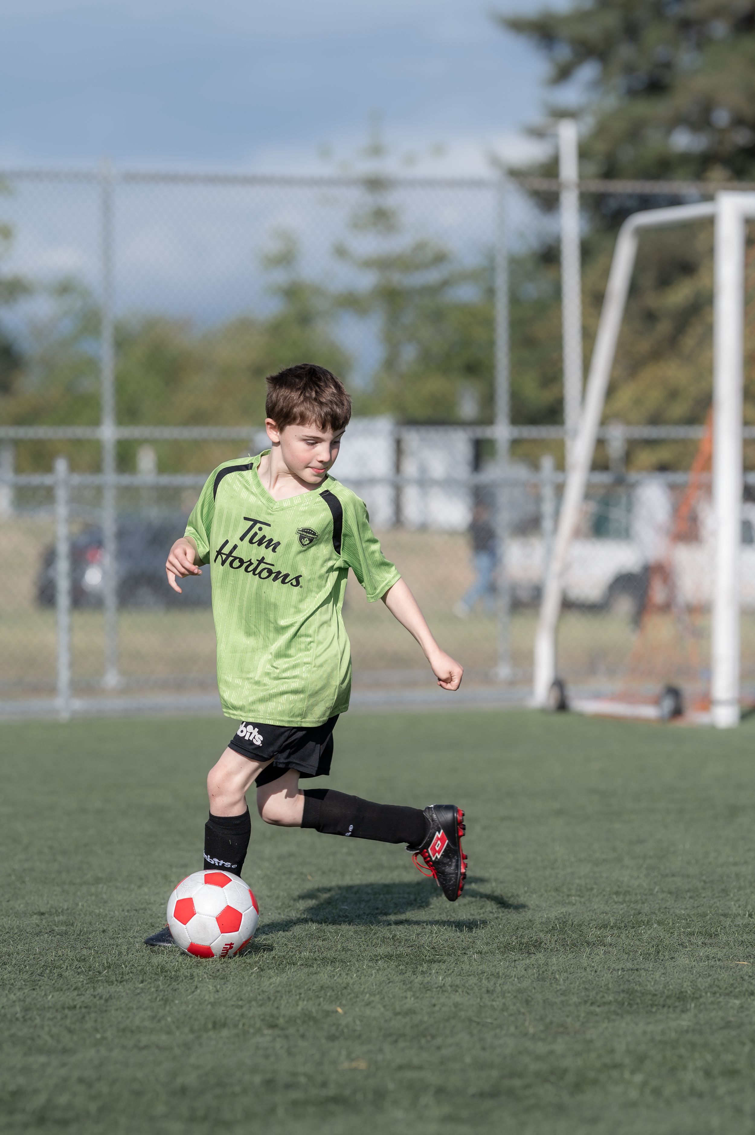 Young boy in green Tim Hortons jersey dribbling a soccer ball on a grass field during a youth soccer game.