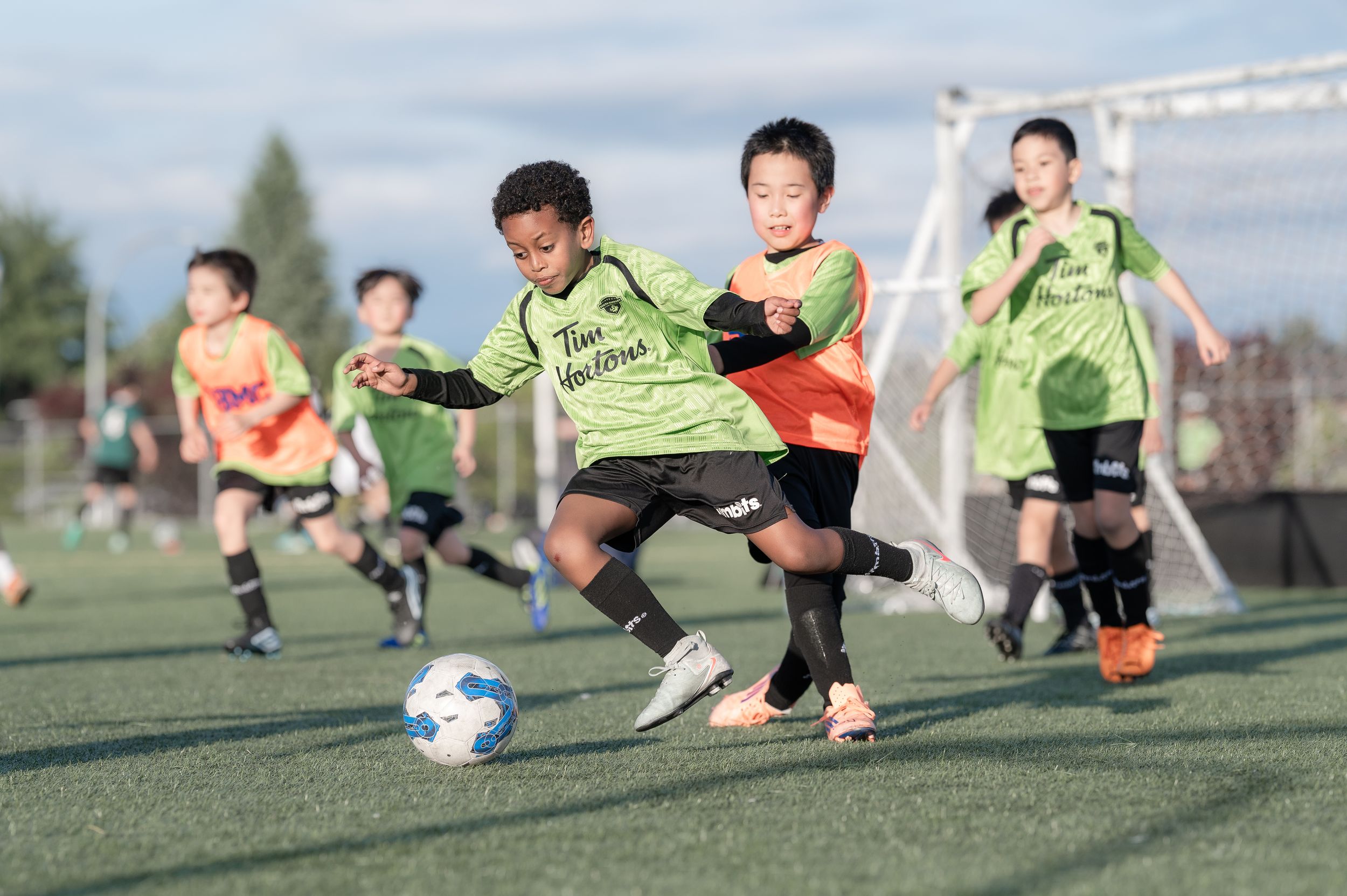 Young boys in green jerseys compete for the ball during an outdoor youth soccer match on a turf field.