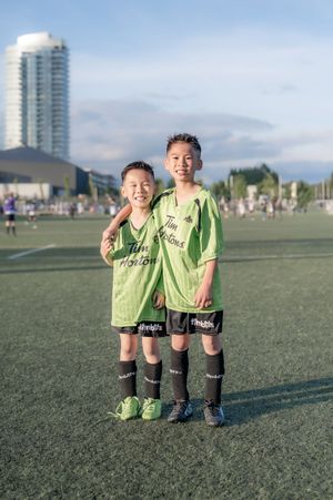 Two smiling boys in green Tim Hortons soccer uniforms pose together on a turf field.