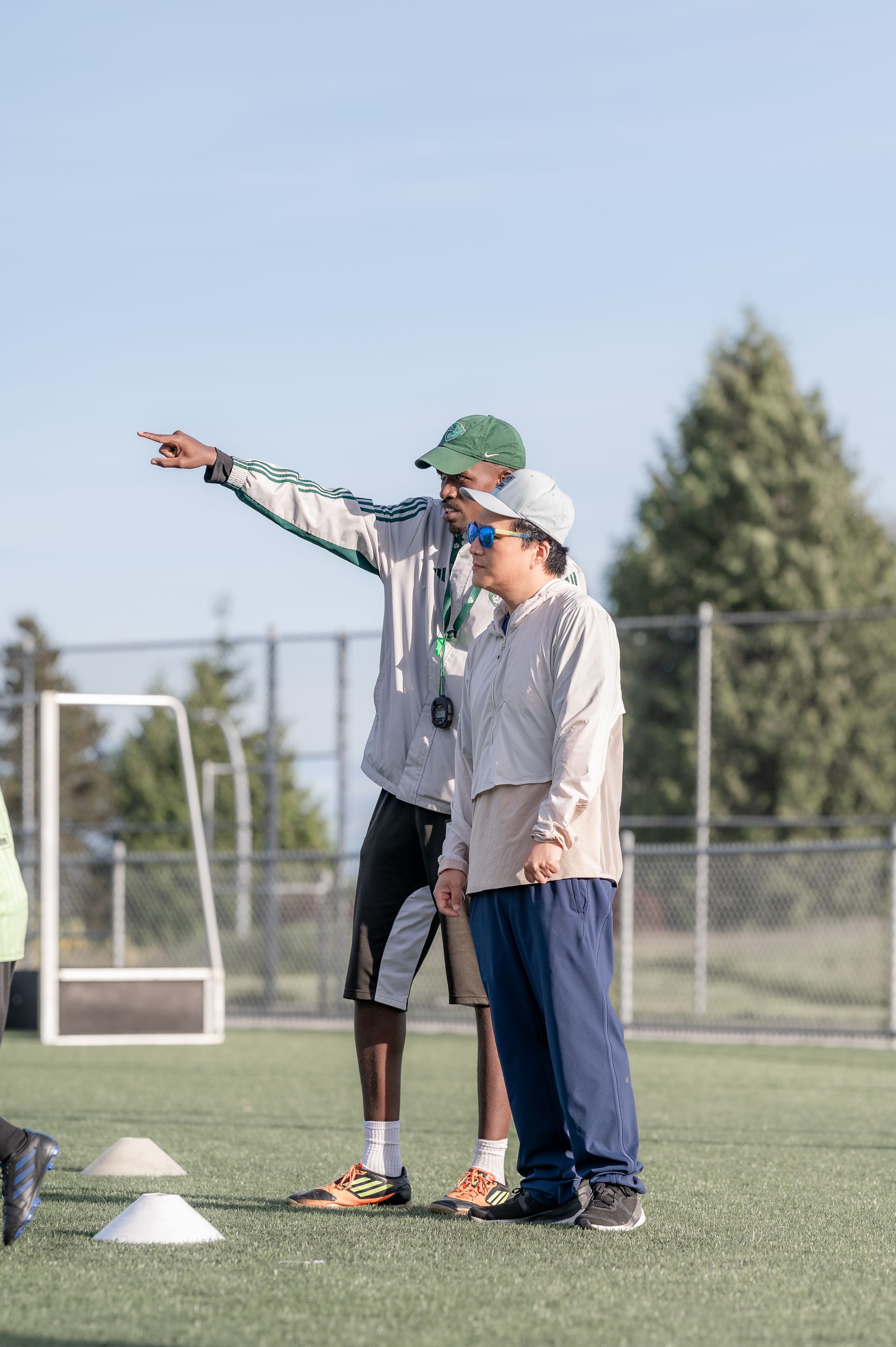 A coach points directions to a young soccer player during practice on a green turf field.