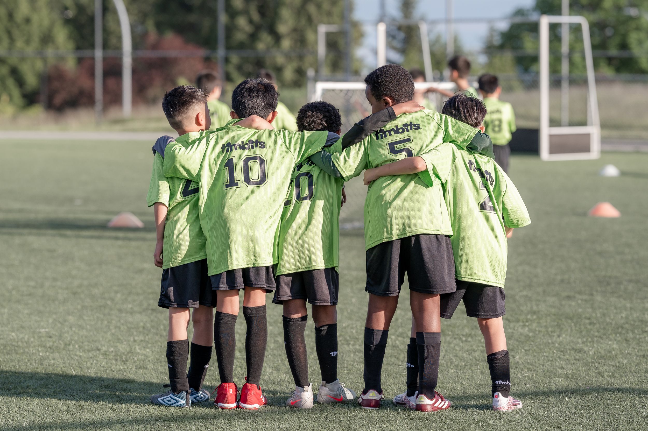 Youth soccer team in green jerseys huddling together on a grass field during a game or practice session.