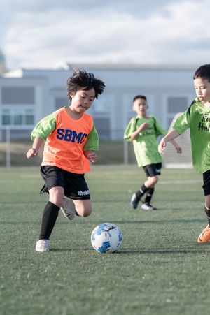 Young children in colorful jerseys compete for the ball during an energetic youth soccer game on a turf field.