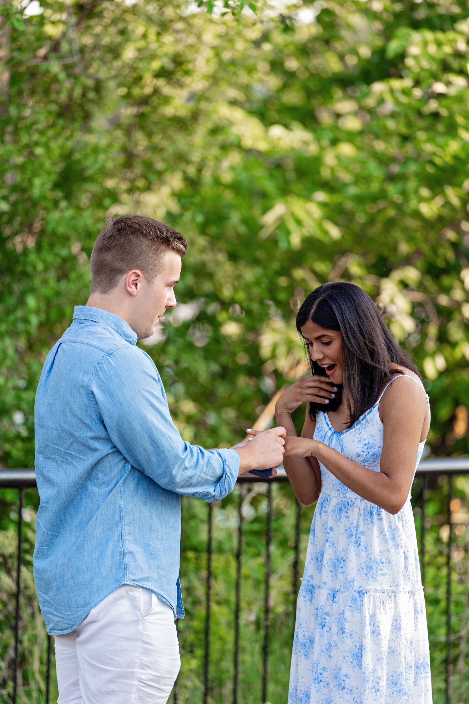 Couple sharing an emotional engagement moment as man places ring on surprised womans finger outdoors.