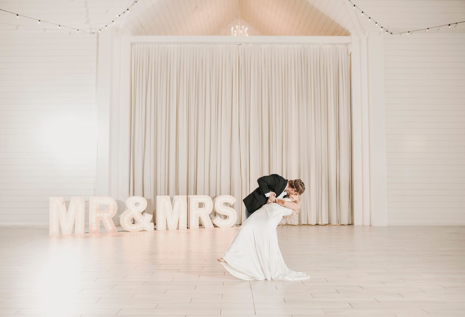 Bride and groom celebrate their wedding day with a dramatic dip kiss surrounded by family and friends