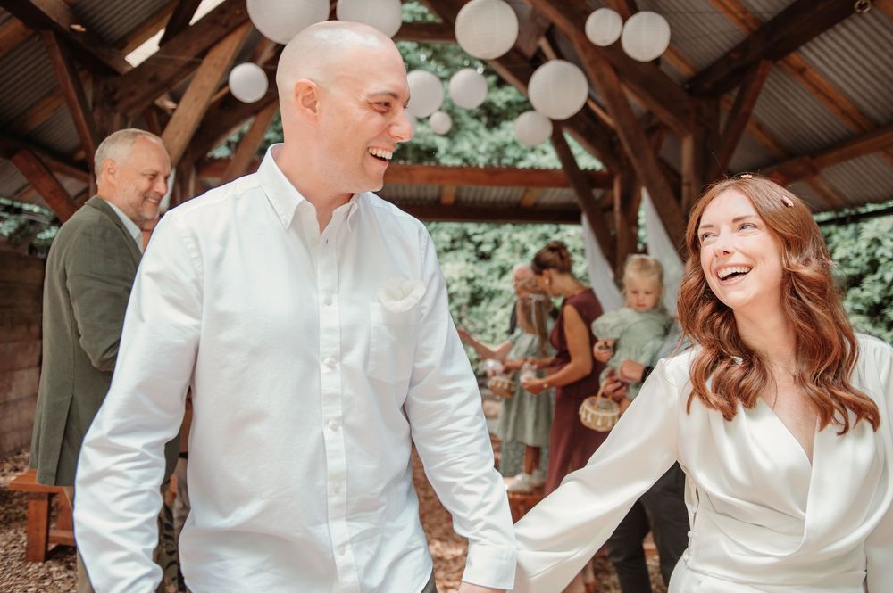 Happy newlywed couple holding hands and laughing at their rustic woodland wedding venue.