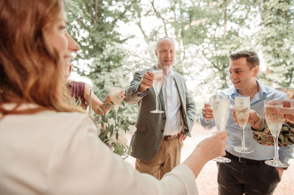 Guests raising glasses in a champagne toast outdoors at a wedding celebration among trees.