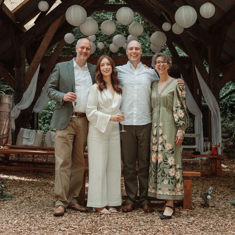 Four adults smiling together at an outdoor wedding venue decorated with paper lanterns and draped fabric.