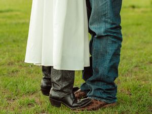 Close-up of couple wearing cowboy boots standing on green grass, white dress visible.