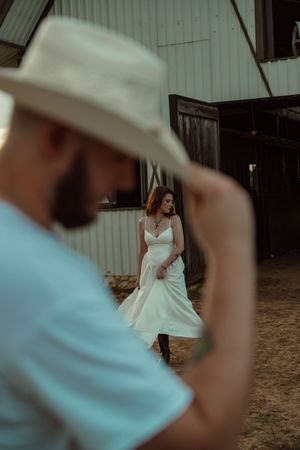 Man in white cowboy hat watches woman in white dress twirl inside a rustic barn.