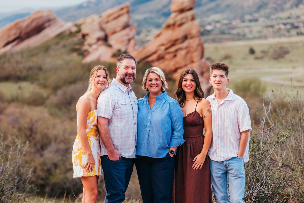 Family of five smiling together outdoors at Red Rocks Park Colorado with scenic red rock formations in background.
