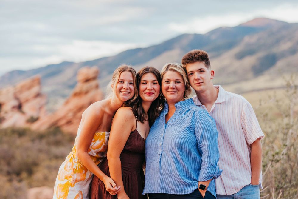 Four smiling family members pose together outdoors with red rocks and mountains in the background.