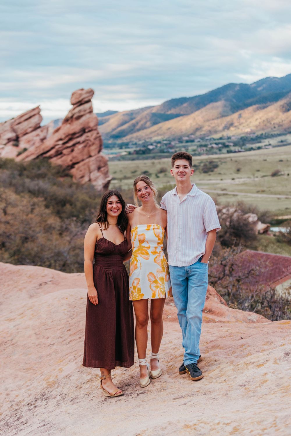 Three young adults posing together on red rocks with mountain backdrop in Colorado.