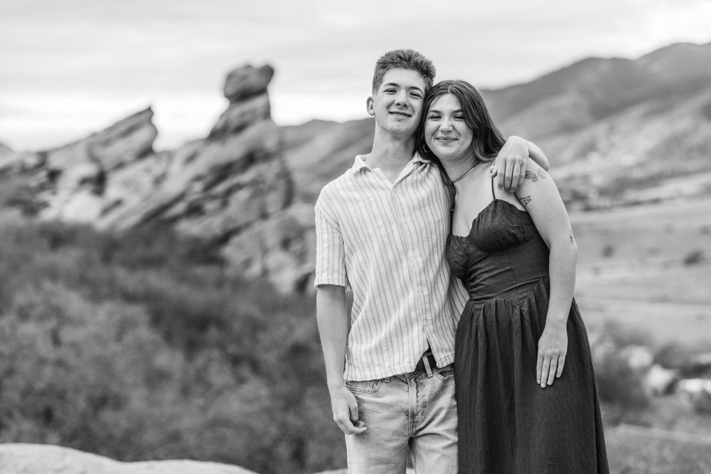 Black and white photo of a young couple smiling at Red Rocks Park, Colorado, with iconic rock formations in the background.