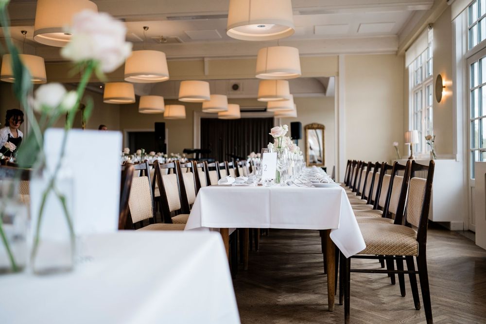 Elegant restaurant dining room with long white tablecloths, dark wooden chairs, and pendant lights for a formal event.