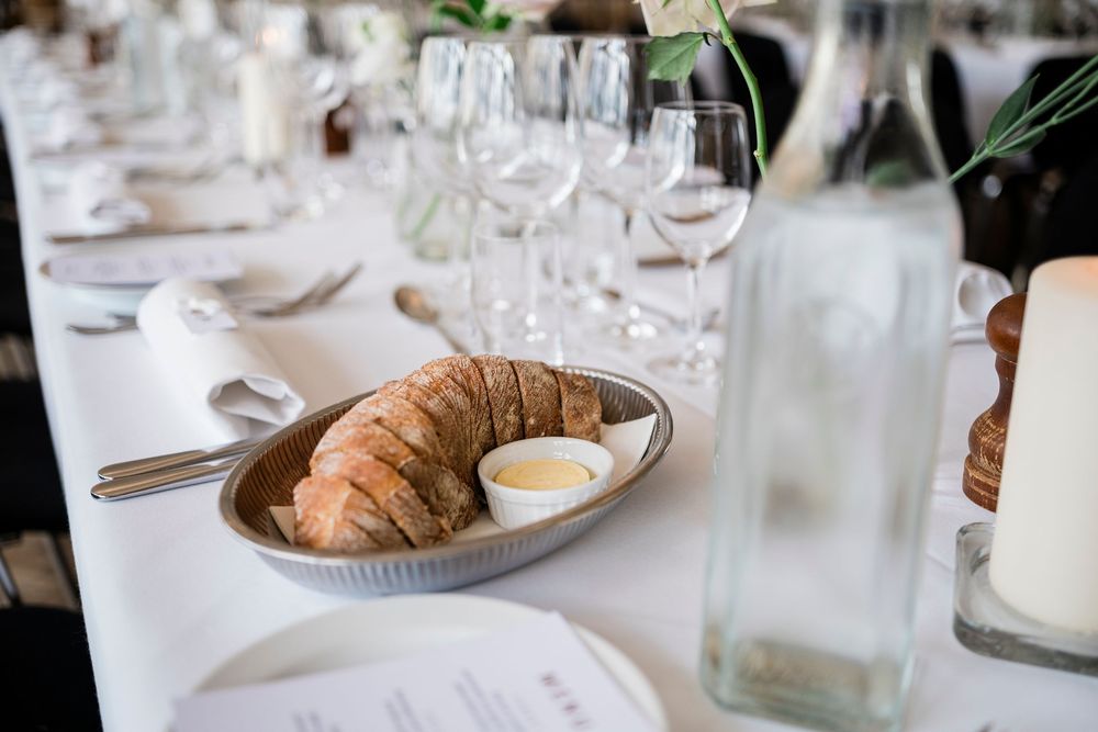 Sliced croissant served in a ceramic dish with dipping sauce on an elegantly set dining table with wine glasses.