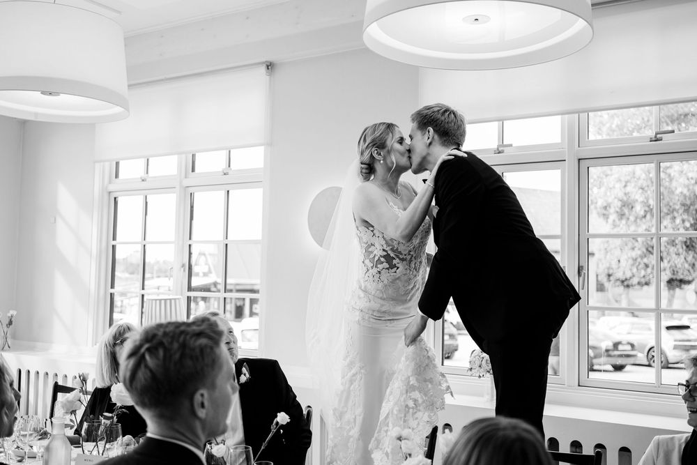 Black and white photo of a bride and groom sharing their first kiss at their wedding reception.