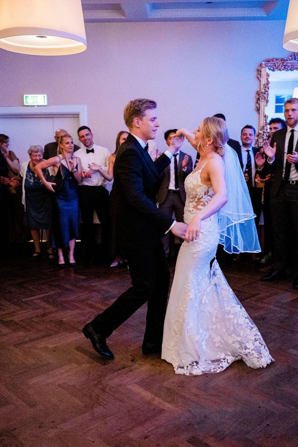 Bride and groom share their first dance at wedding reception while guests celebrate in background.