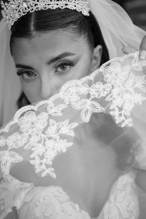 Black and white close-up of bride with crystal tiara peering over intricate floral lace wedding veil.