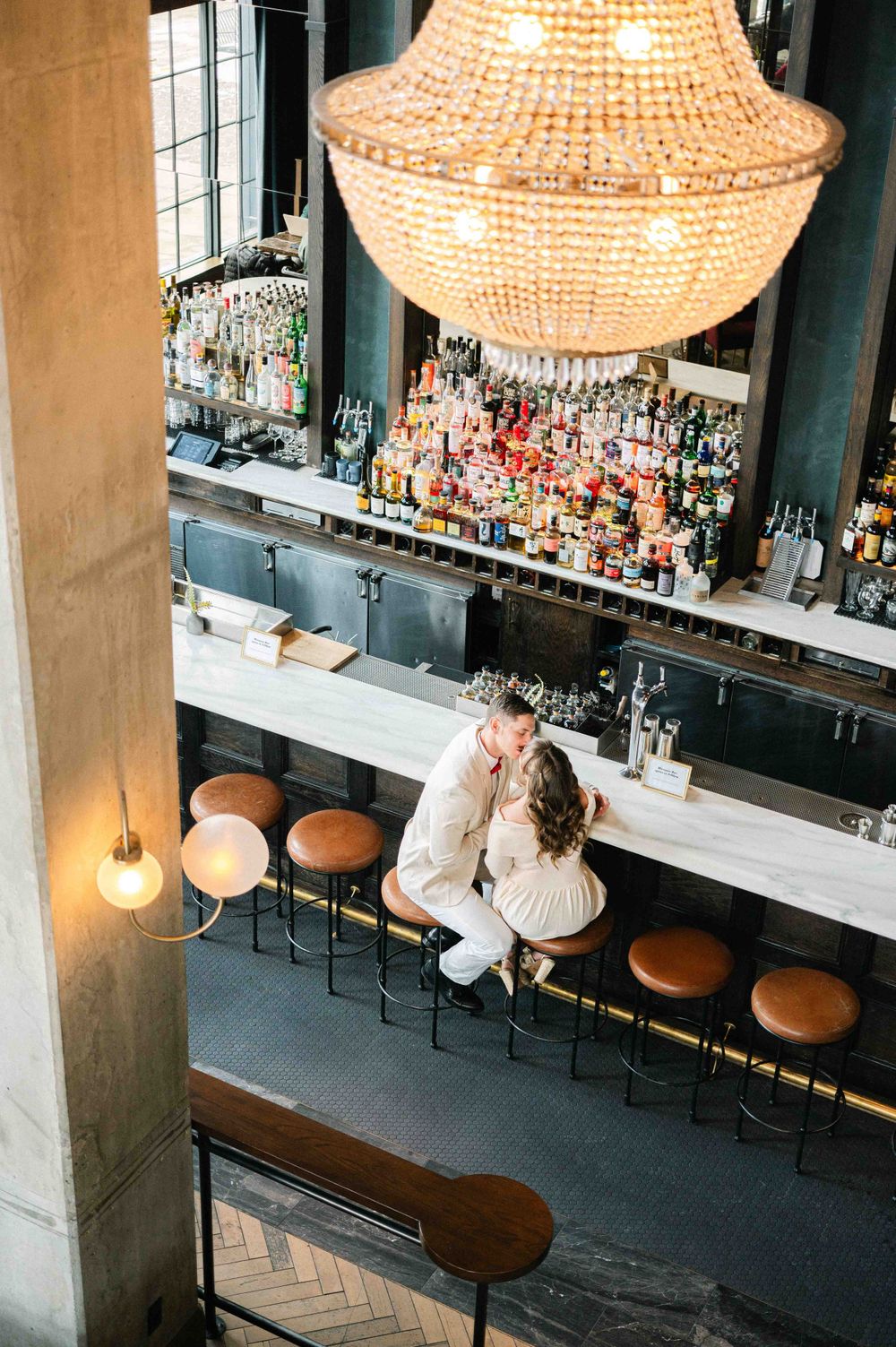 A romantic scene at an upscale bar with a crystal chandelier and extensive liquor display.