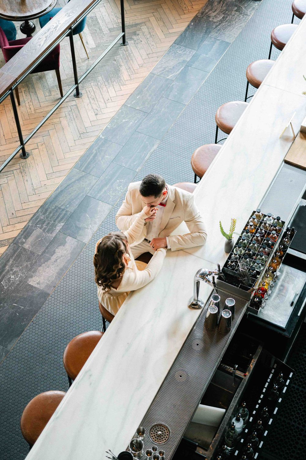 A birds-eye view of a couple sharing an intimate moment at a long marble bar counter.