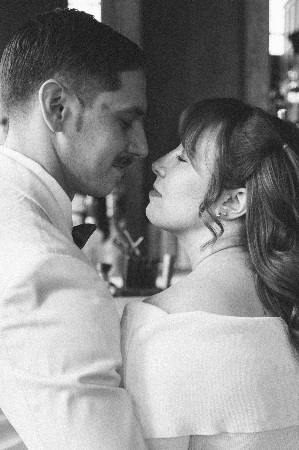 An intimate black and white portrait of a couple in cream-colored formal attire.