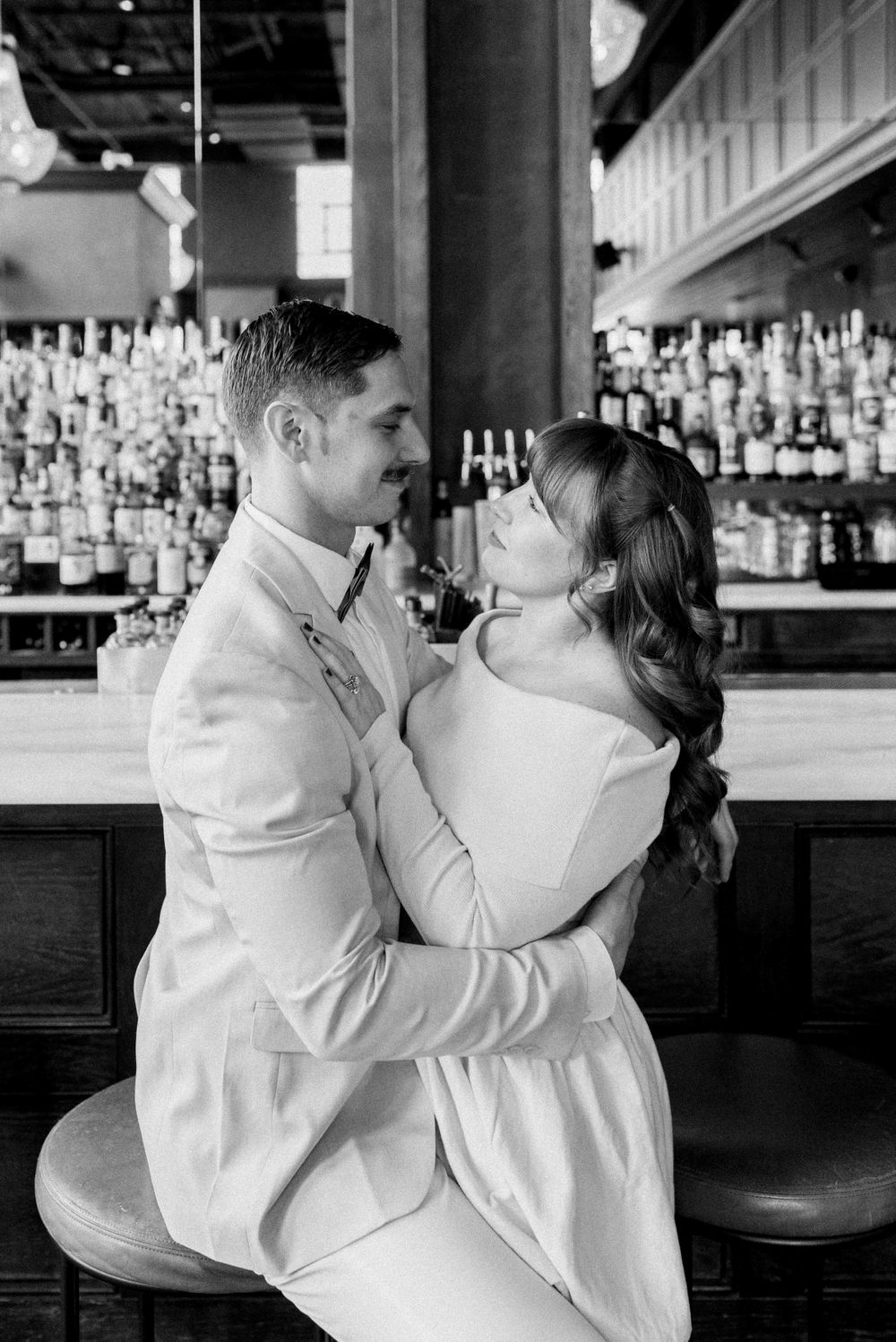 A black and white photo of an intimate moment at a bar with bottles displayed in background.