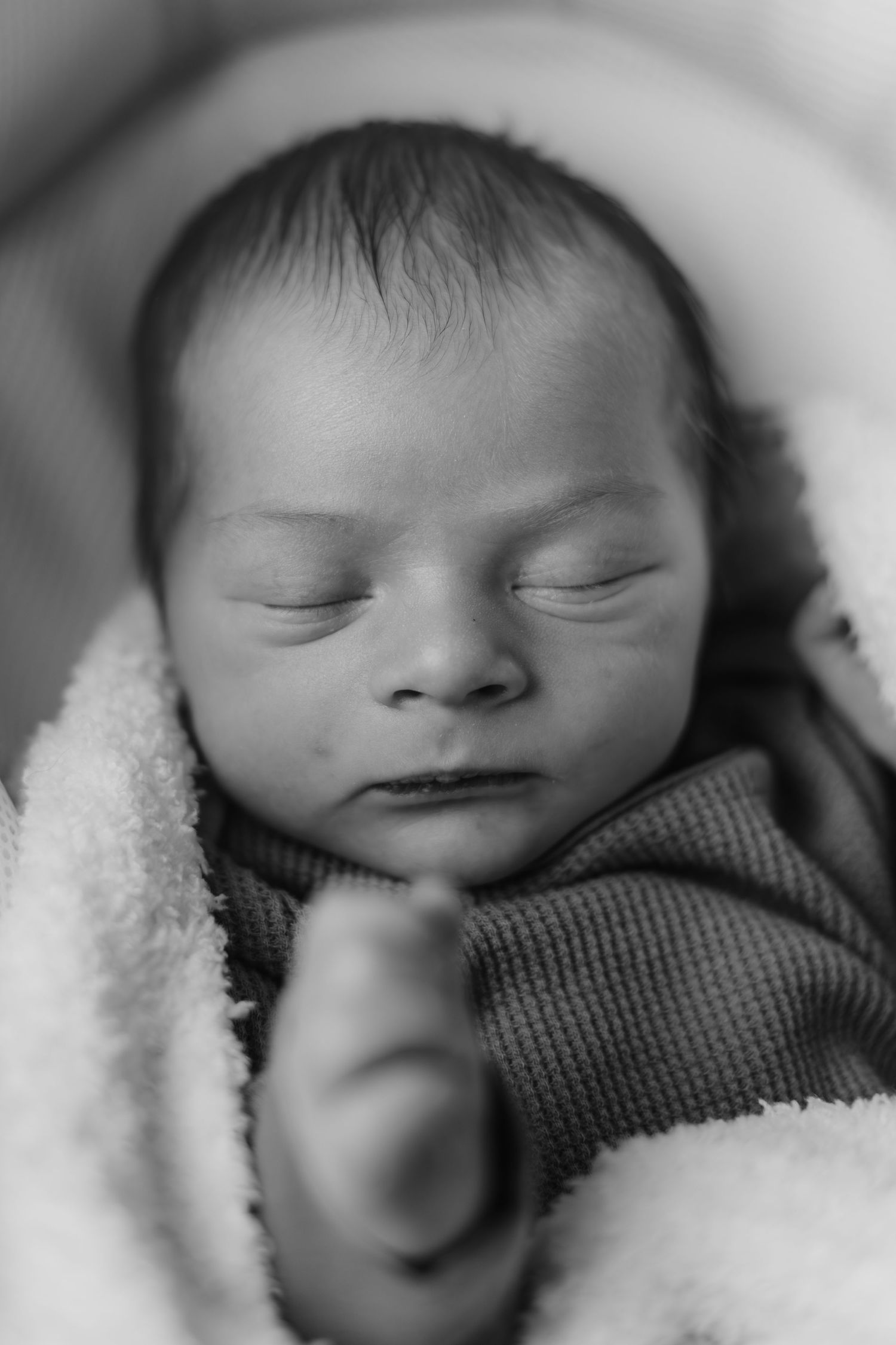 Sleeping newborn wrapped in soft blankets in black and white.