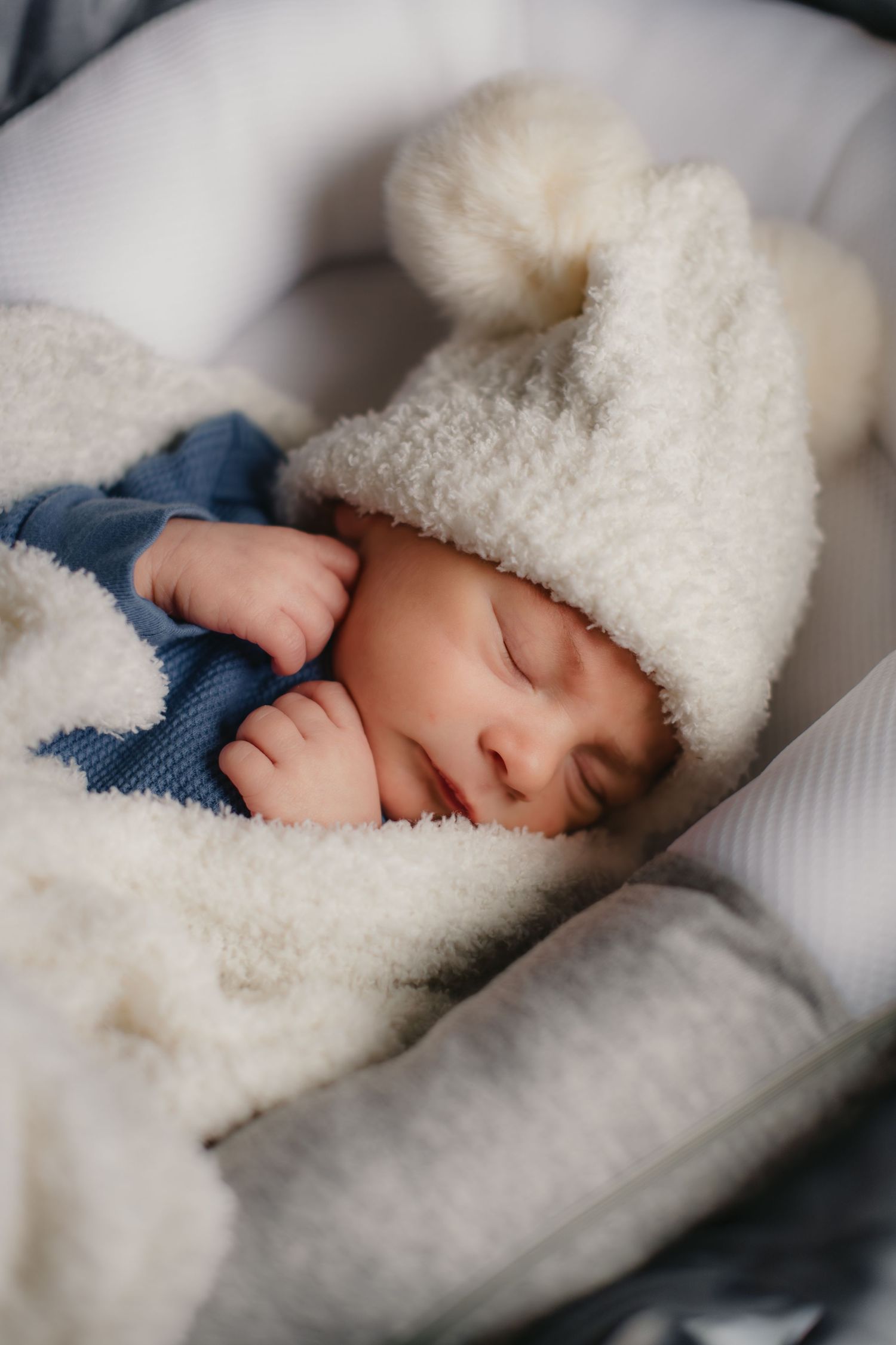 Peaceful sleeping baby wearing fluffy white winter hat.