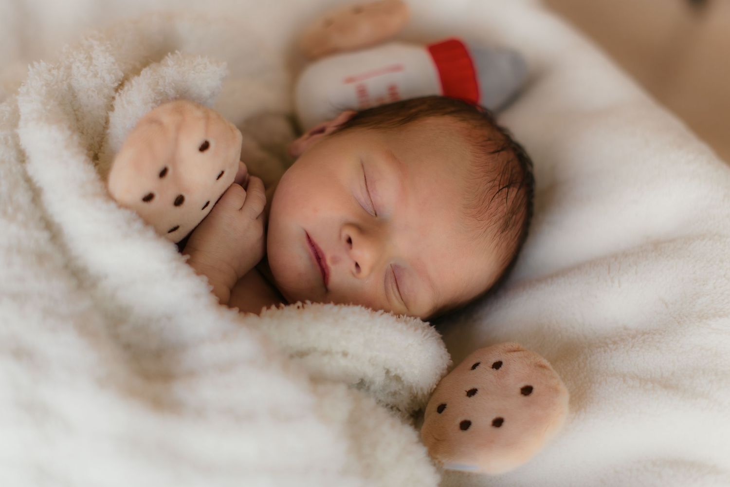 Peaceful sleeping newborn cuddled with teddy bear on white blanket.