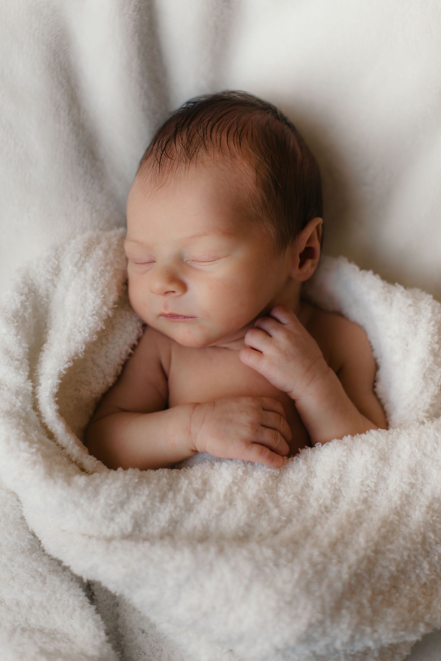 Serene newborn sleeping in soft white blanket with crossed arms.