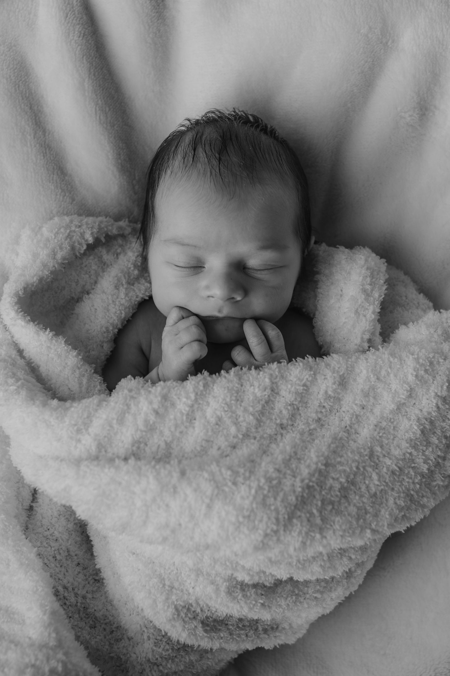Black and white image of sleeping newborn swaddled in textured blanket.