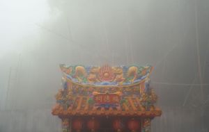 Ornate Chinese temple roof detail shrouded in thick fog.