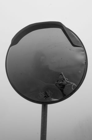 Black and white convex traffic mirror reflecting a foggy landscape.