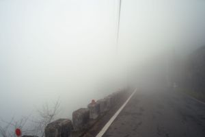Foggy mountain road with stone barriers disappearing into the mist.