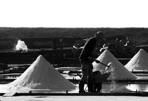 Black and white photo of salt mounds at a mining operation with workers in silhouette.
