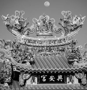 Ornate Chinese temple roof decorations under a full moon.