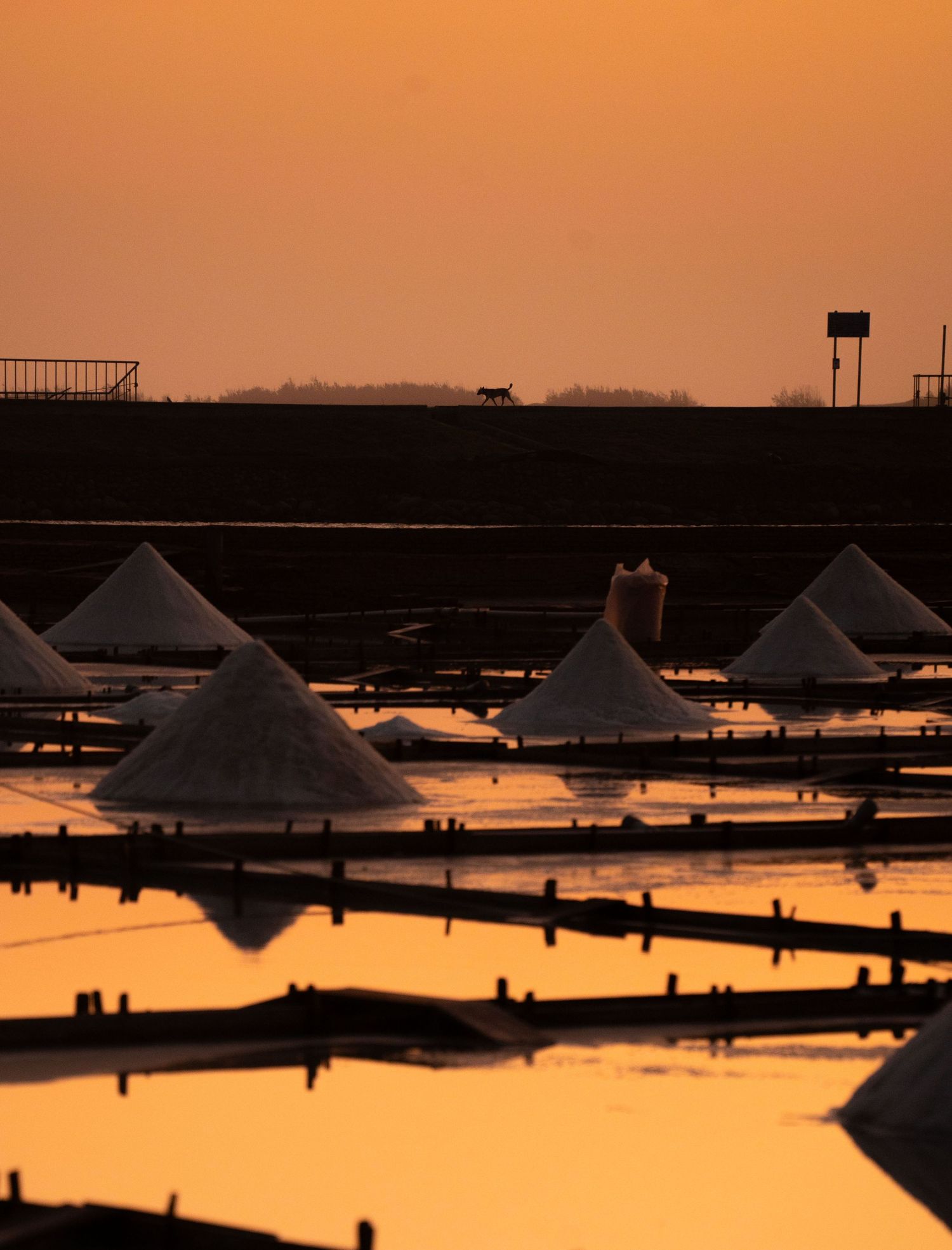 Industrial salt production ponds with pyramid-shaped mounds silhouetted at dusk.