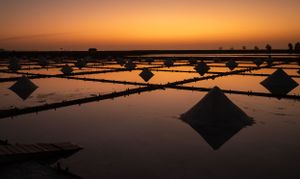 Salt pyramids casting reflections in shallow water basins during golden hour.