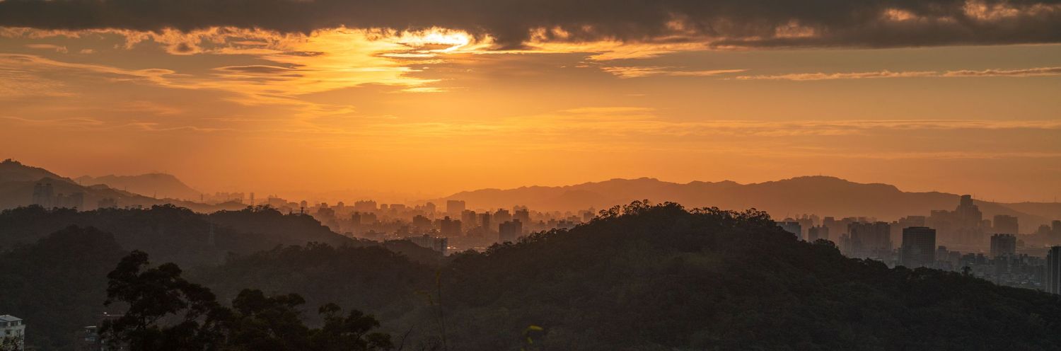 Golden sunset sky over mountain ranges and city buildings.
