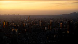 Dramatic sunset view over a sprawling city with mountains silhouetted in the distance.