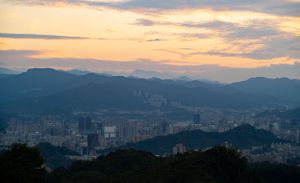 Aerial view of a city nestled between mountains during golden hour with dramatic clouds overhead.