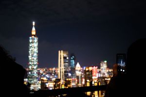 Blurred nighttime cityscape featuring the illuminated Taipei 101 tower and surrounding buildings.