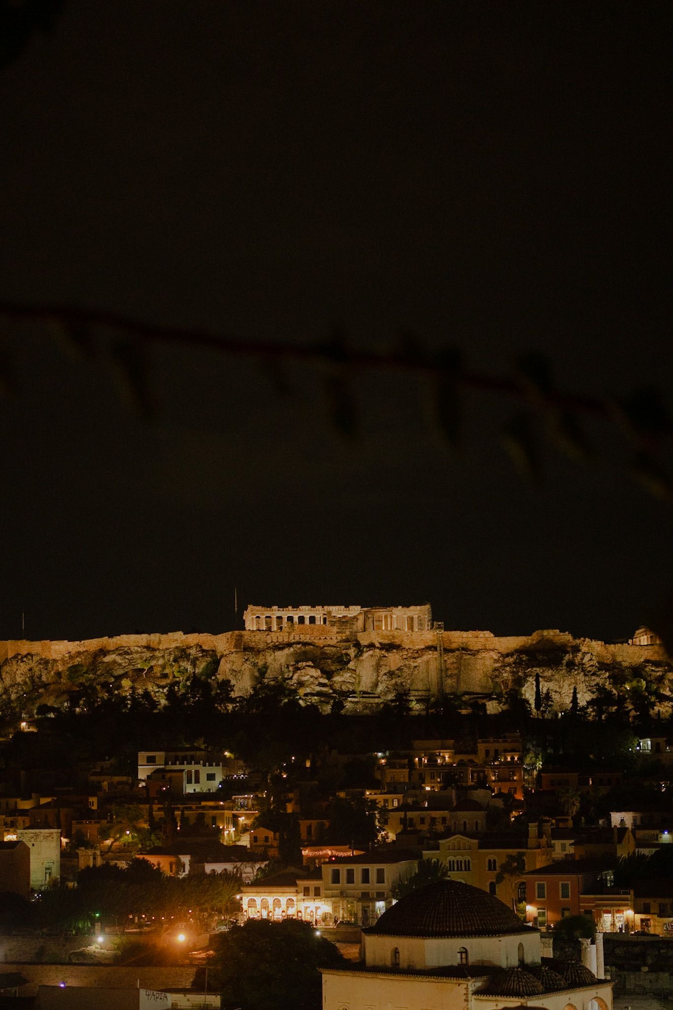 The illuminated Acropolis stands majestically atop a hill overlooking Athens at night with city lights glowing below.