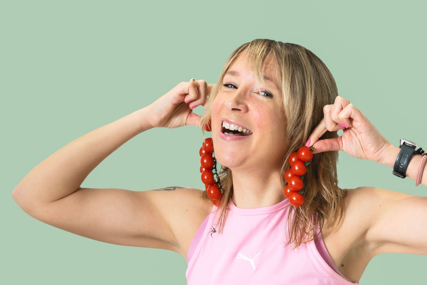 smiling woman holds up cherry tomatoes as earrings on a green background