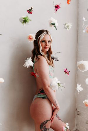 Artistic boudoir photo with floating flowers and soft lighting against a white wall.