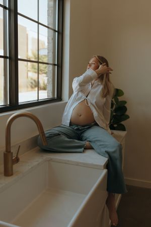 Silhouetted person in casual attire sits on white countertop by window with natural light streaming in.
