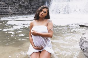 Person in a white dress poses near a waterfall in a moody outdoor portrait session.